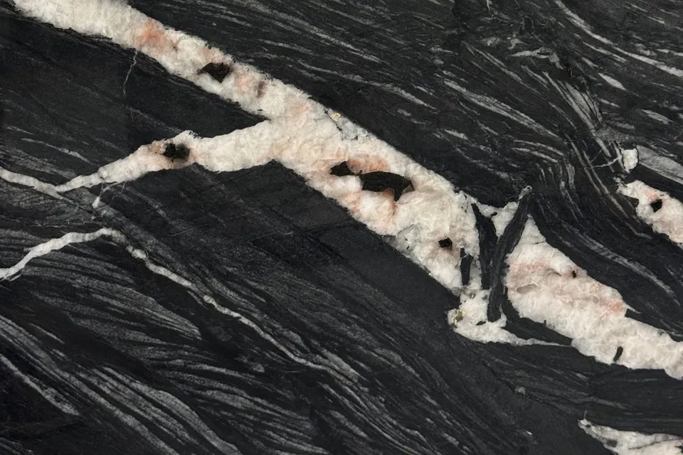 Black slab with flowing wavy white lines and a wide pink and white crystal seam