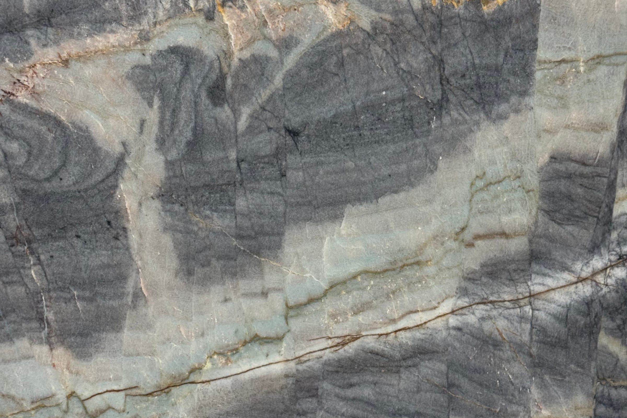 Dark gray cloudy patches on pale sage stone with thin brown and gold veins
