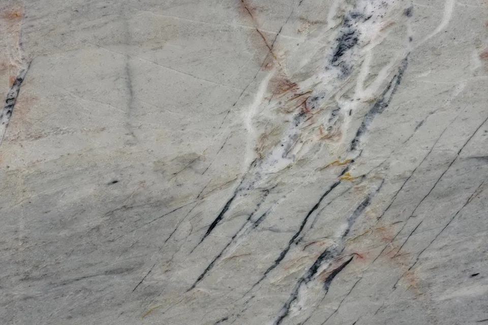 Sage gray-green stone with fine dark fracture lines and thin rust-red and white veins
