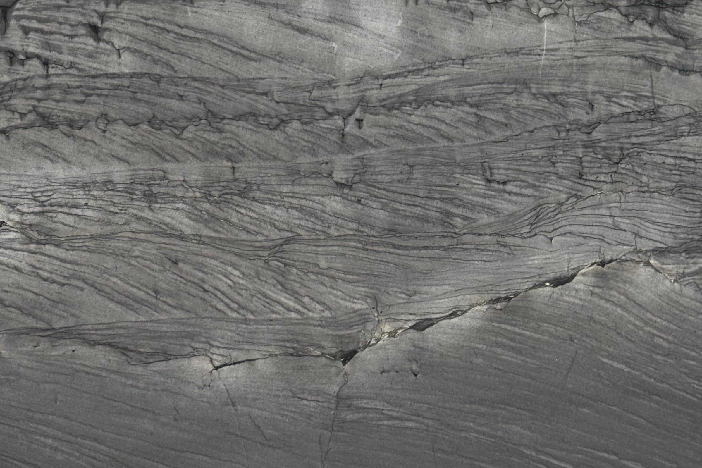 Dark gray layered stone with a textured surface and dense thin black lines running horizontally