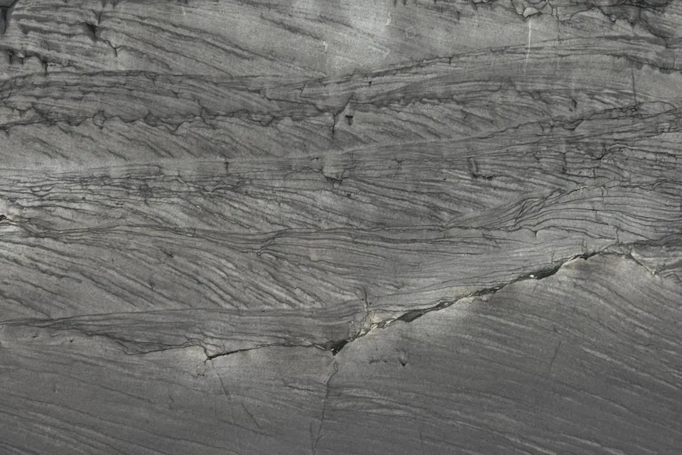 Dark gray layered stone with a textured surface and dense thin black lines running horizontally