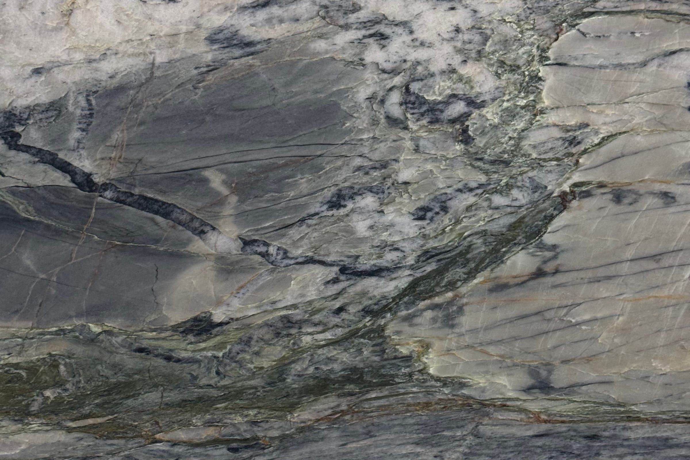 Gray and cream stone with darker gray clouded areas and thin rust and green seams