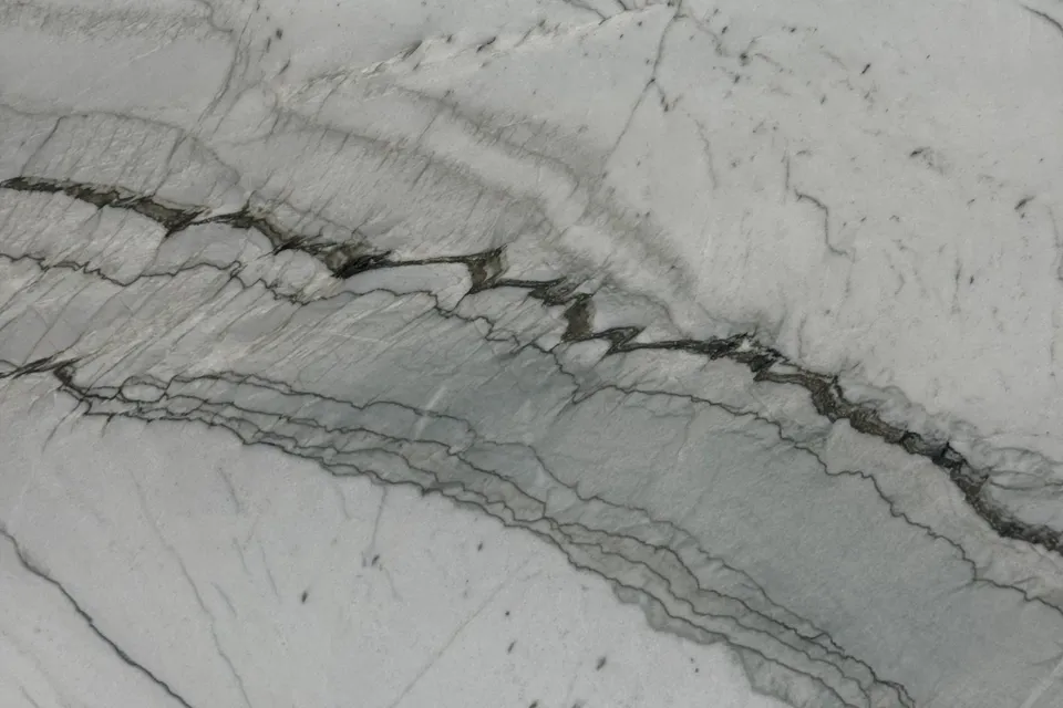 White-gray stone with thin dark linear veins and layered bands running across the slab