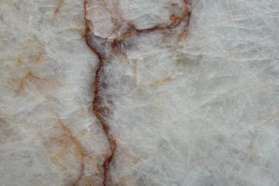 Translucent white crystalline stone with thin red and orange veins branching across it